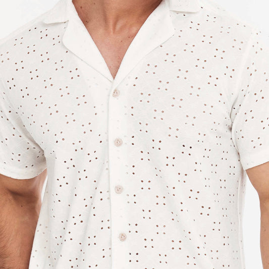 A man wearing a white short-sleeved button-up shirt with a camp collar, paired with dark swim shorts. Shirt is in English Embroidery style, embroidered resort shirts