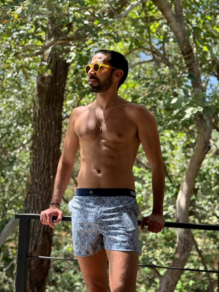 Man wearing sunglasses and patterned shorts standing outdoors with trees in the background. swim shorts for men