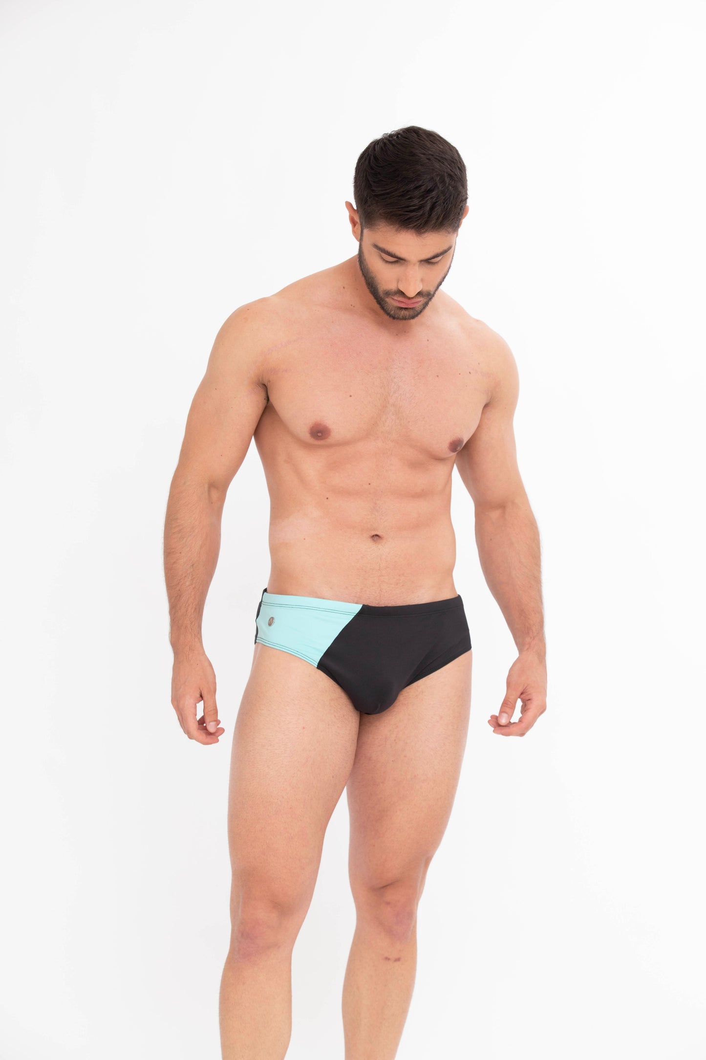 Man wearing black swim briefs with a light blue patch on a white background. luxury men’s swimsuits