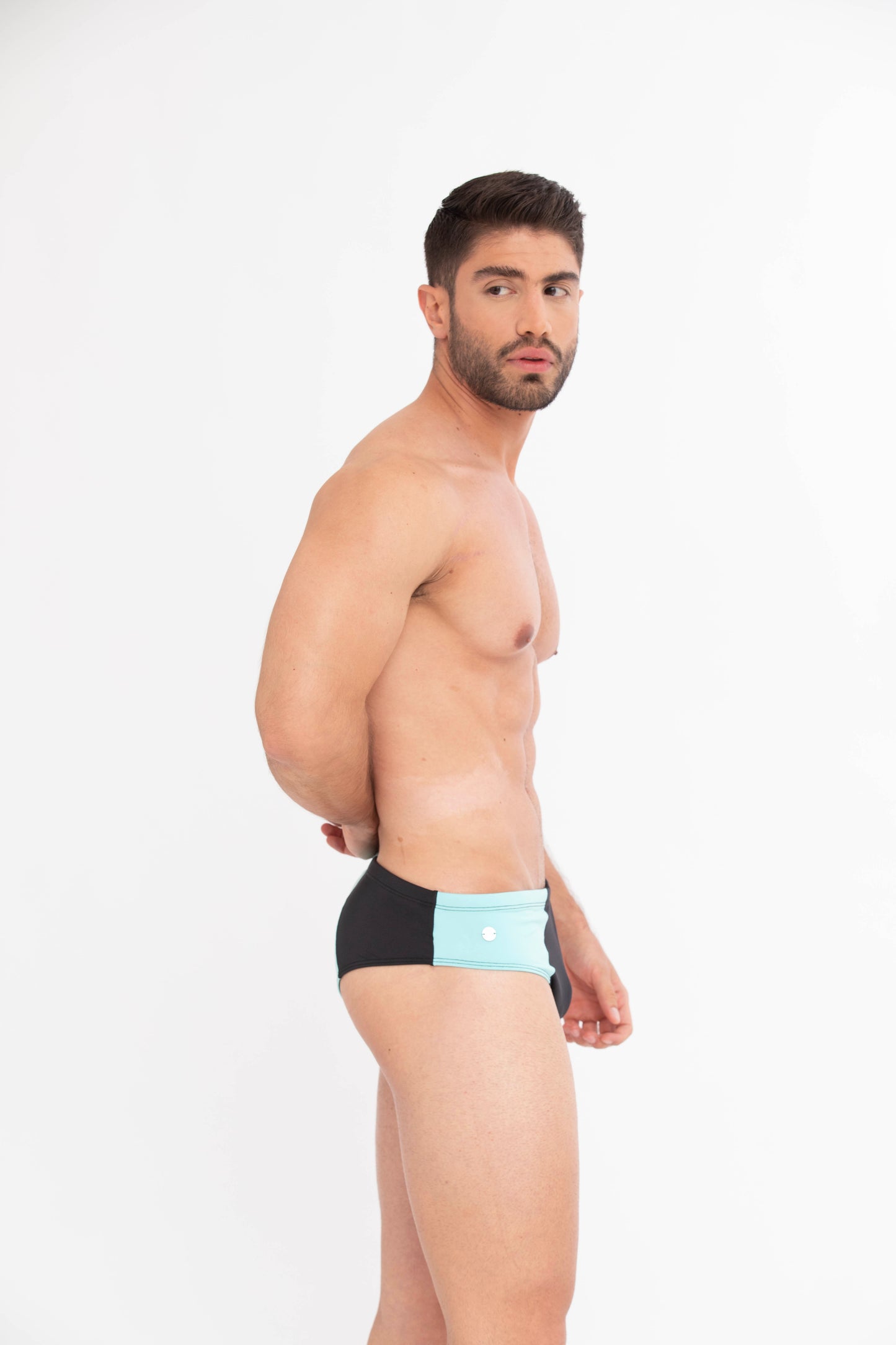 Man wearing black swim briefs with a light blue patch on a white background. luxury men’s swimsuits