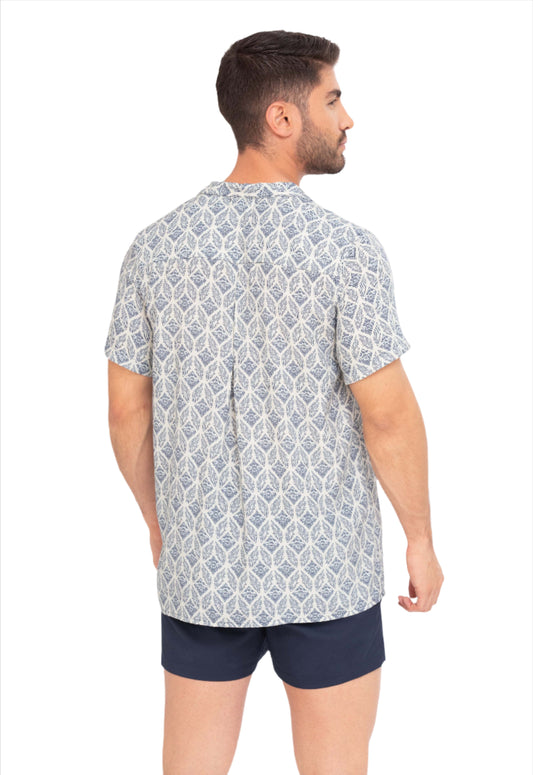A man wearing a short-sleeved camp collar shirt with a geometric pattern in blue and white colors and matching swim shorts. lightweight summer shirts. aegean mosaic print