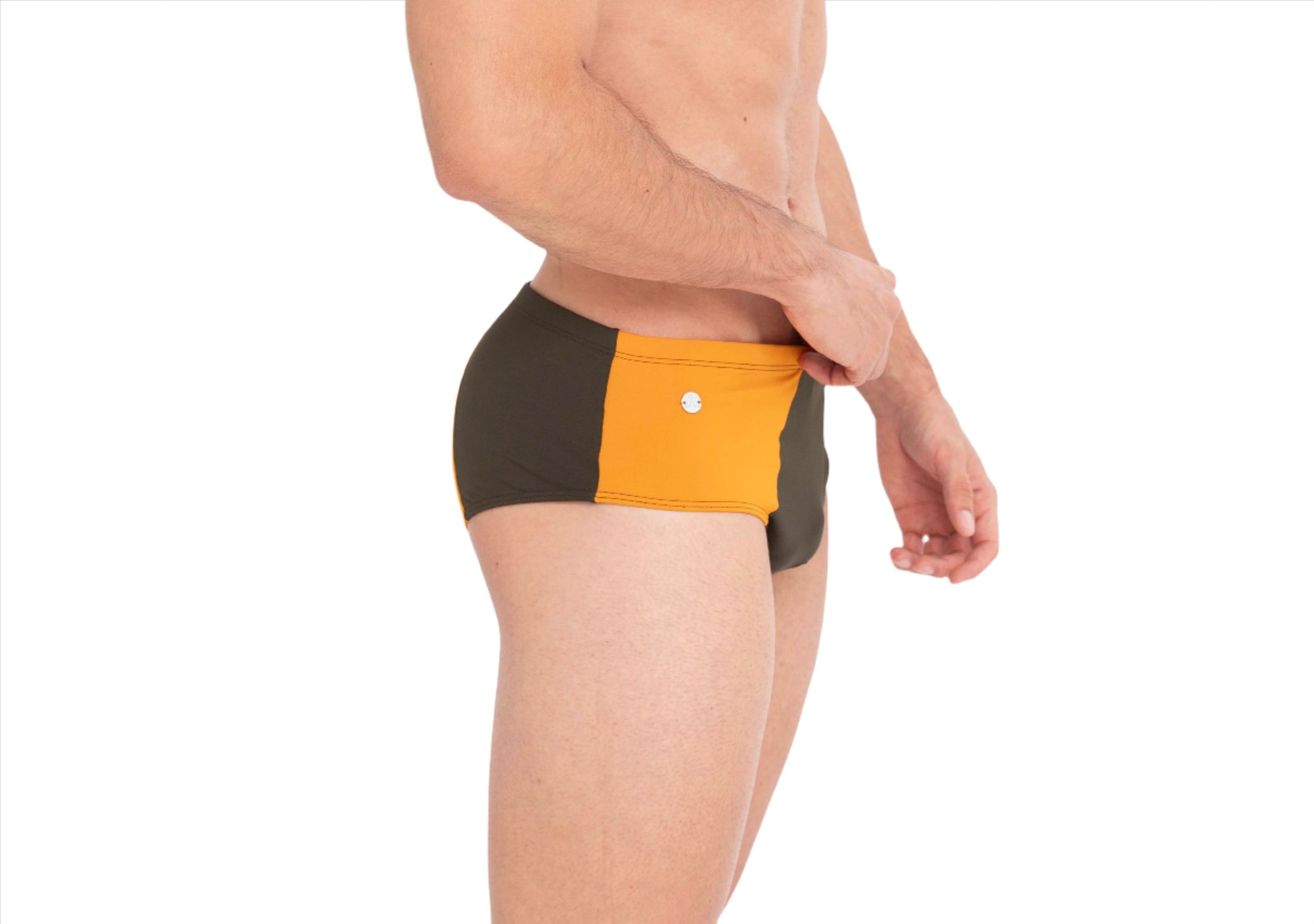This image features a male model sporting The Athletic Swim Brief, inspired by the vibrant sunsets over Albufeira, Portugal. The swimsuit is designed with a striking color block pattern in sunset orange and olive green, set against a more muted green waistband.