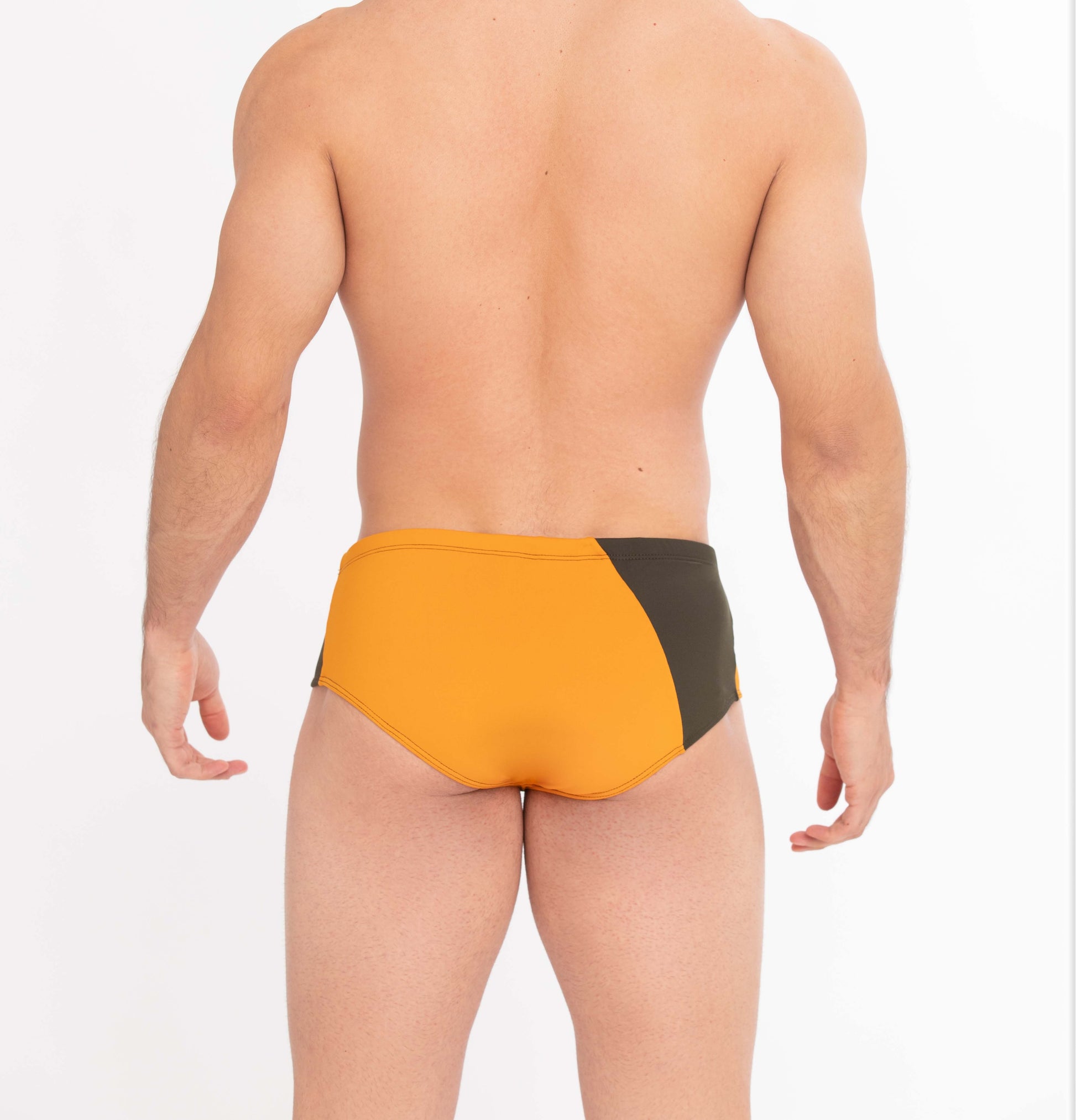 This image features a male model sporting The Athletic Swim Brief, inspired by the vibrant sunsets over Albufeira, Portugal. The swimsuit is designed with a striking color block pattern in sunset orange and olive green, set against a more muted green waistband.